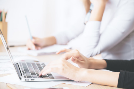 Close up of businesslady's hands using laptop computer placed on messy office desktopの写真素材