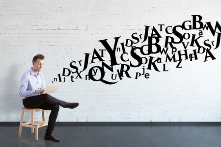 businessman sitting on chair and holding laptop, letters drawn behind him. Concept of studyingの写真素材