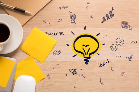 Top view of wooden desktop with creative light bulb drawing, business icons, stickers, coffee cup...