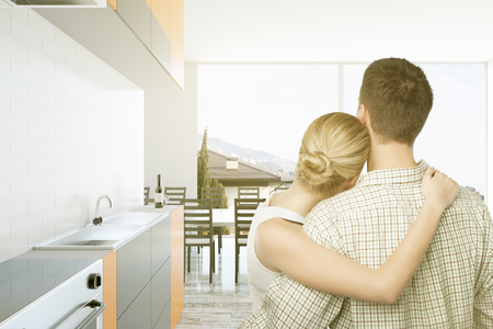 Back view of cuddling caucasian couple in bright kitchen interior. They are thinking about the future of their familyの写真素材