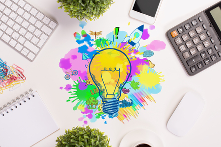 Top view of white office desktop with various items and colorful lamp and rocket sketch. Creative startup ideasの写真素材