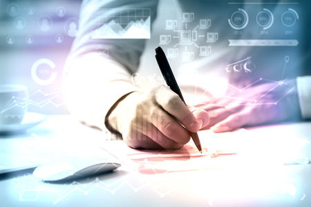 Close up of man doing paperwork at workplace with creative business charts and diagrams. Toned image. Accounting conceptの写真素材
