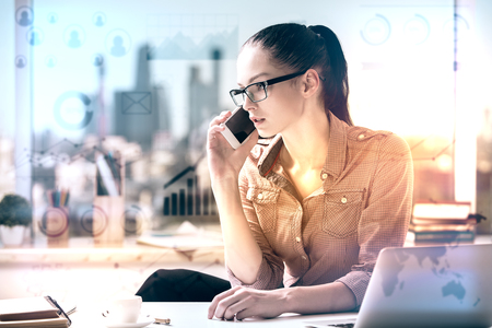 Attractive caucasian woman at workpace with abstract business charts talking on the phone and working on project. Finance concept. Toned imageの写真素材