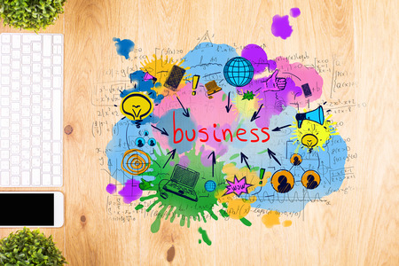 Top view of wooden desktop with colorful business sketch, smartphone, keyboard and decorative plantsの写真素材