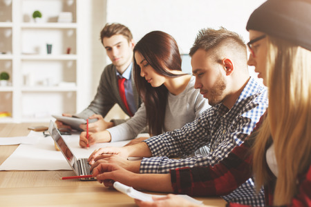 Beautiful caucasian businesspeople at workplace looking at laptop screen together. Team working on project. Teamwork conceptの写真素材