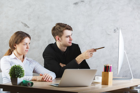 Handsome businessman explaining something to female colleague, pointing at computer screen in modern office. Teamworkの写真素材