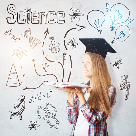 Attractive cheerful young caucasian woman with open book, drawn mortarboard and other education related drawings. Intellect conceptの写真素材