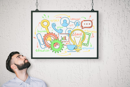 Young businessman with business drawing in frame. Concrete background. Communication concept