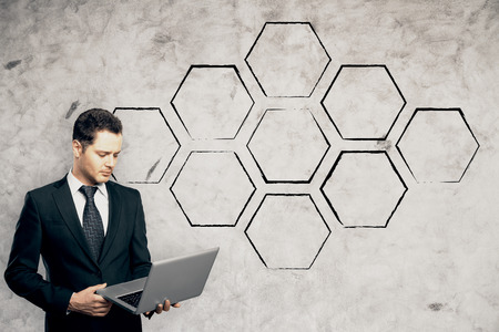 Handsome young businessman using notebook on concrete wall background with abstract drawn cells. Copy space. Technology conceptの写真素材