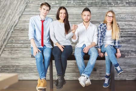 Four young caucasian businesspeople sitting on table in wooden interior and holding hands. Teamwork conceptの写真素材