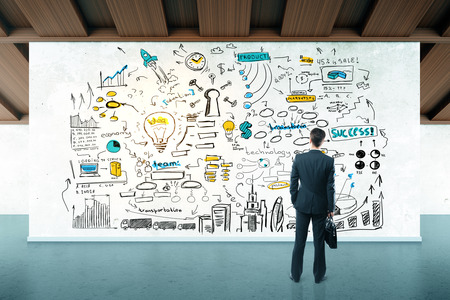 Back view of thoughtful businessman in modern interior looking at wall/billboard with colorful business sketch. Teamwork concept. 3D Renderingの写真素材
