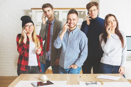 Group of beautiful smiling guys and girls in office talking on their phones all at once. Communication conceptの写真素材