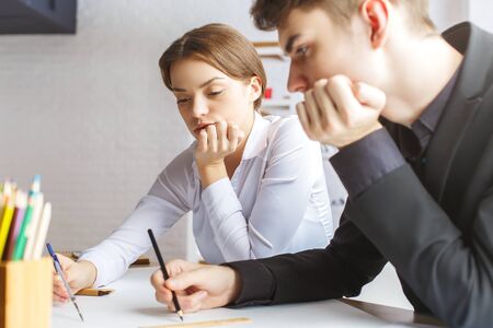 Side view of attractive young european guy and girl doing paperwork at workplace. Teamwork conceptの写真素材