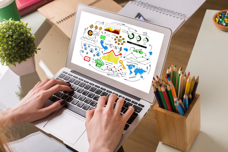 Female hands using laptop with colorful business sketch. Workplace with plant, pencil pot and other supplies in the background. Communication conceptの写真素材