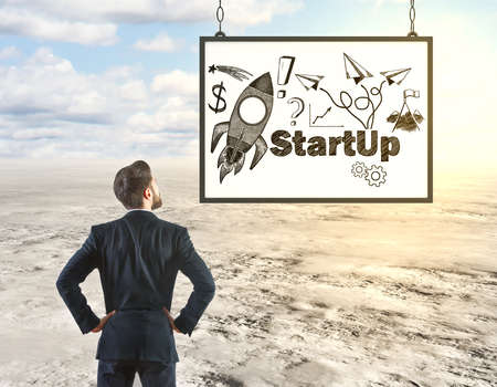 Back view of young businessman looking at frame with rocket doodle on desert background. Start up conceptの写真素材