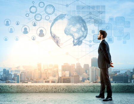 Side view of handsome young man standing on rooftop with digital charts, globe, HR and other icons. City view background. International business concept