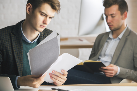Portrait of handsome caucasian man working on project at workplace. Blurry colleague reading book in the backgroundの写真素材