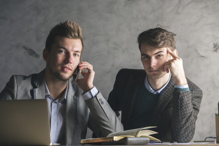 Close up of two cheerful caucasian gentlemen talking on the phone and doing paperwork in modern office. Teamwork conceptの写真素材