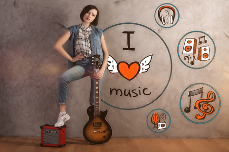 Attractive young woman with guitar and foot on amplifier standing in interior with sketch on concrete wall. Music lover conceptの写真素材