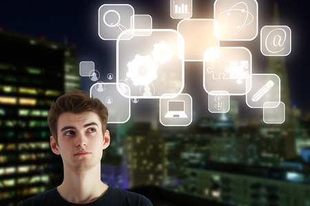 Handsome thoughtful young businessman on night city background with business icons in cells. Research conceptの写真素材