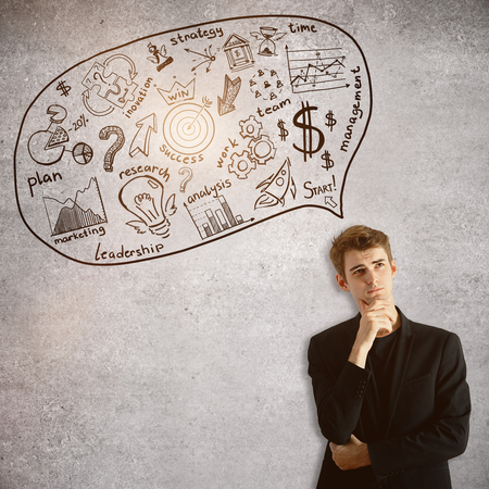 Handsome young businessman on concrete background thinking about business. Management concept