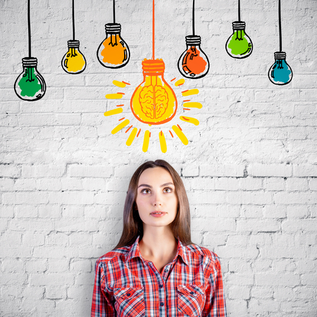 Portrait of attractive thoughtful european girl on brick background with drawn light bulbs. Idea conceptの写真素材