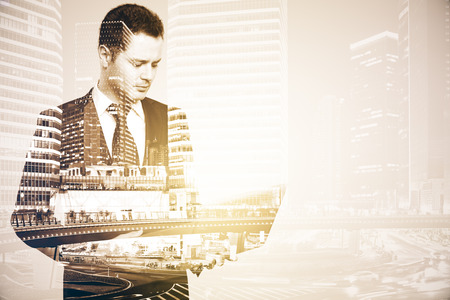 Portrait of handsome businessman using laptop on abstract city background with copy space. Technology and communication concept. Double exposureの写真素材