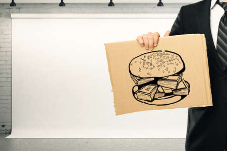 Young businessman holding carboard with dollar bill burger in brick interior with poster. Money concept. 3D Renderingの写真素材