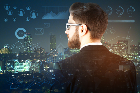 Back view of young businessman on city background with abstract business icons and charts. Finance concept. Double exposureの写真素材