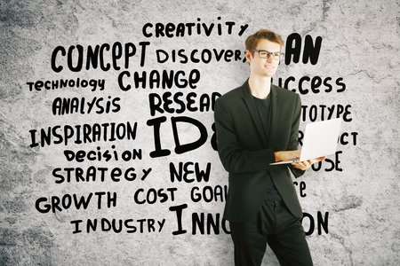 Cheerful young businessman using laptop on concrete background with text. Success conceptの写真素材