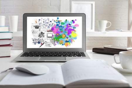 Close up of office desktop with colorful sketch on laptop screen, open diary, coffee cup, books and other items. Creative and analytical thinking conceptの写真素材