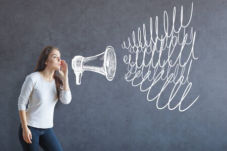Woman whispering into megaphone on textured concrete background. Communication conceptの写真素材