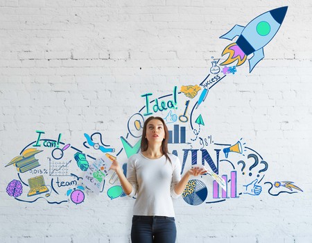 Confused young woman with paperwork in hands standing on white brick background with spaceship sketch. Start up conceptの写真素材