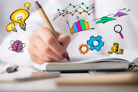 Close up of female hands writing in notepad with colorful business icons. Creative idea conceptの写真素材