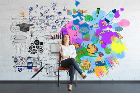 Thoughtful young woman sitting on chair in brick interior with colorful sketch on wall. Creative and analytical thinking conceptの写真素材