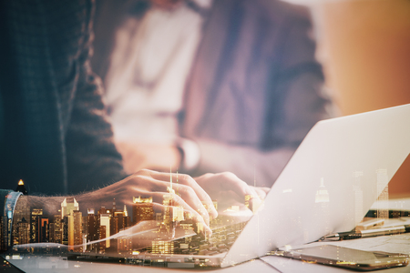 Side view and close up of male hands typing on laptop keyboard. Abstract night city background. Communication concept. Double exposureの写真素材