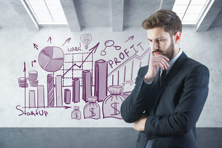Side view of attractive thoughtful young businessman in concrete interior with business drawings on wall. Finance concept. 3D Renderingの写真素材