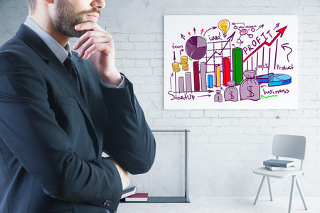 Side view of attractive thoughtful young businessman in brick interior with business drawings on wall. Profit concept. 3D Renderingの写真素材