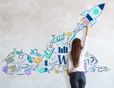 Back view of young woman drawing rocket sketch on concrete wall. Startup conceptの写真素材