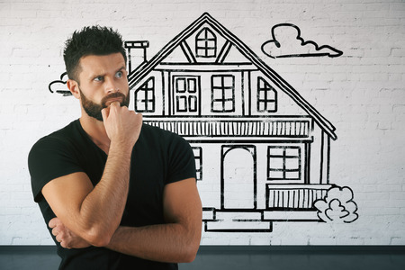 Thoughtful bearded young man in brick interior with drawn house. Real estate and mortgage concept. 3D Renderingの写真素材