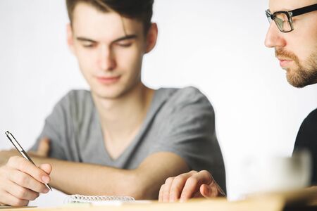 Portrait of handsome young males doing paperwork in modern office with blurry coffee cup and other items. Teamwork conceptの写真素材