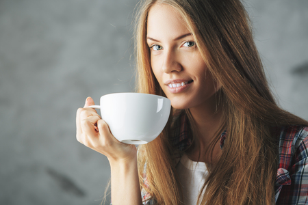 Close up portrait of attractive european woman drinking coffee out of large mugの写真素材