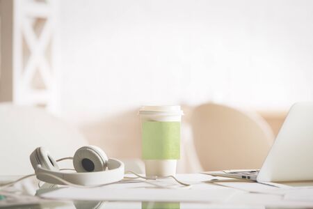 Close up of bright worlplace with headphones, laptop and green sticker on take away coffee cup. Mock upの写真素材