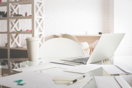 Close up of office desktop with coffee cup, paperwork, laptop and other items