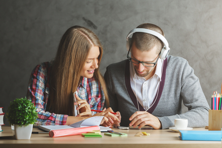 Attractive white businessman and woman working on creative project together. They are using electronic devices and listening to music through at workplaceの写真素材