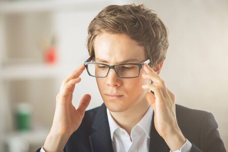 Close up portrait of thoughtful young european guy with glasses at workplace
