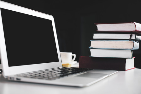 Side view of laptop with blank screen placed on white desktop with book pile and coffee cup. Mock upの写真素材