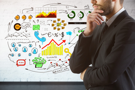 Thoughtful businessman on brick background with colorful business sketch. Communication conceptの写真素材