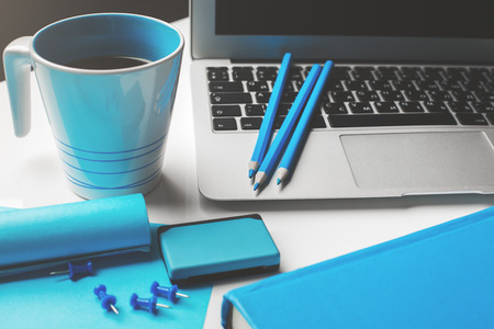 Close up of white desktop with blue supplies, coffee mug, laptop and copy spaceの写真素材