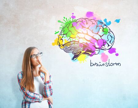 Thoughtful young woman on concrete background with colorful brain sketch. Creative mind conceptの写真素材